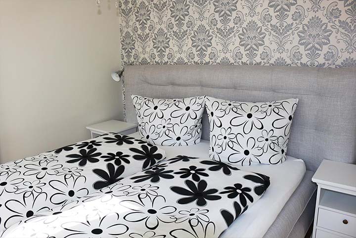 Schlafzimmer, graue Ornamente auf weißer Tapete, Bett mit schwarz-weißer Blumenbettwäsche