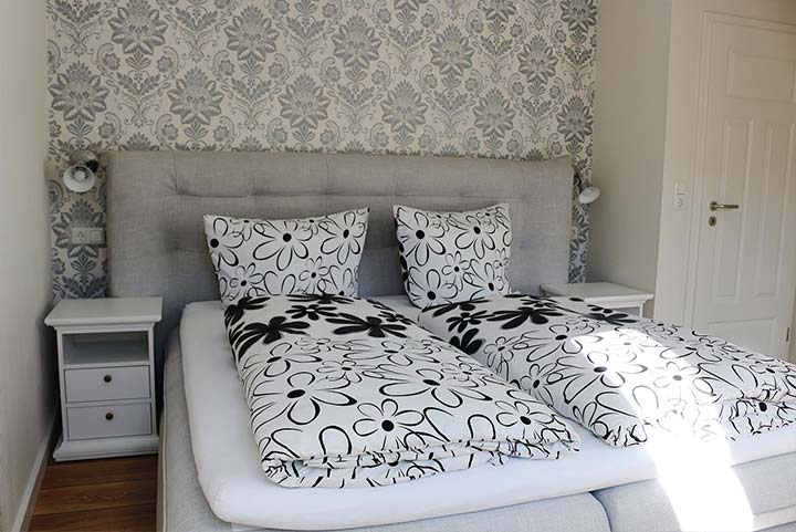 Schlafzimmer, graue Ornamente auf weißer Tapete, Bett mit schwarz-weißer Blumenbettwäsche