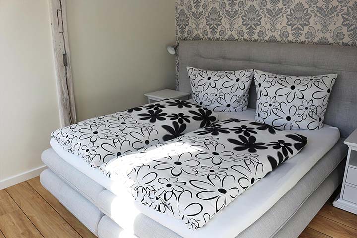 Schlafzimmer, graue Ornamente auf weißer Tapete, Bett mit schwarz-weißer Blumenbettwäsche