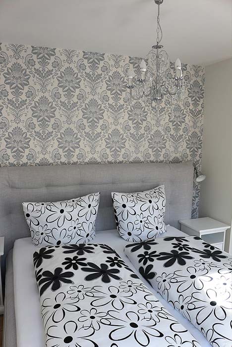 Schlafzimmer, graue Ornamente auf weißer Tapete, Bett mit schwarz-weißer Blumenbettwäsche